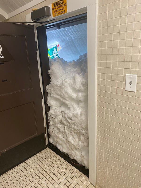 Exit door from a restroom is open, showing snow depth of about 3/4 of the doorframe