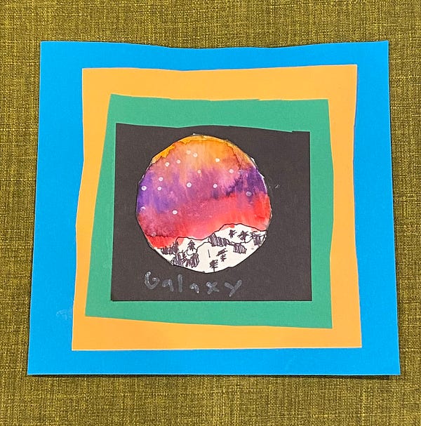 A kid’s art project depicts a “galaxy” with a tree-populated mountain range and a starry purple-orange-red sky, on a square of black construction paper glued to a larger square of green construction paper, glued to a larger square of orange construction paper, glued to a larger square of blue construction paper.