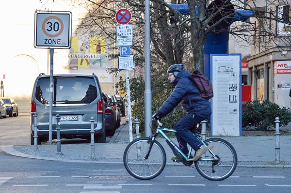 A man on a bicycle in winter attire travels past a large “30 km/hr Zone” sign in Berlin.
