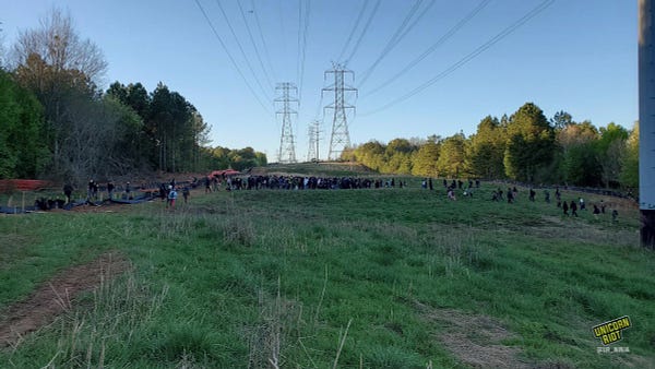 Crowd of hundreds on a power line clearing near proposed Cop City site