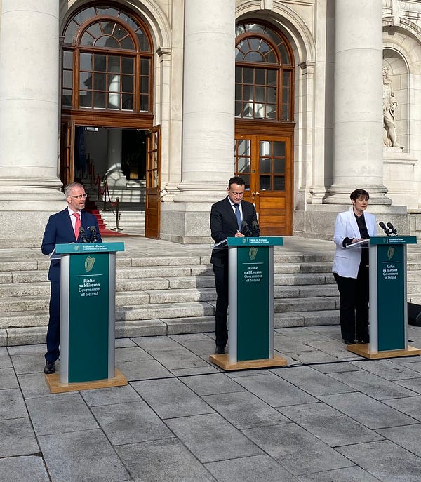 Minister O’Gorman, the Taoiseach and Minister Foley speaking at podiums during a press conference in front of Government Buildings.