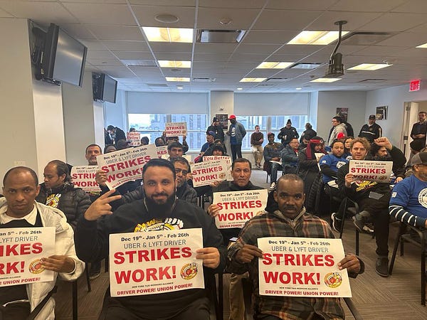 Hearing room with uber and Lyft drivers who are members of NYTWA holding signs that say strikes work
