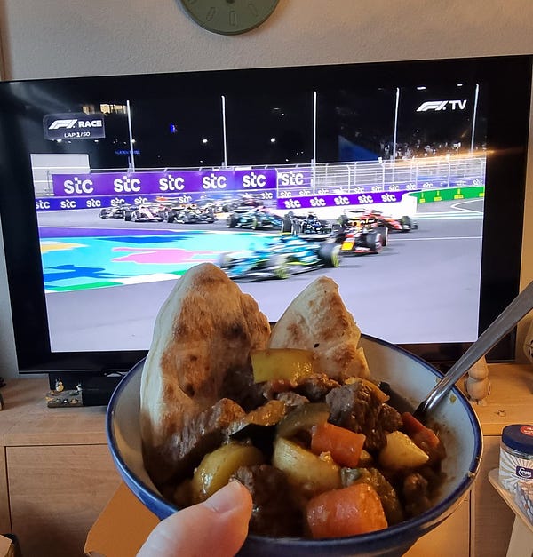 A bowl of Tharid made with beef instead of lamb with two pieces of unleavened bread held in front of a TV showing the opening lap of the Saudi Arabian F1 grand prix