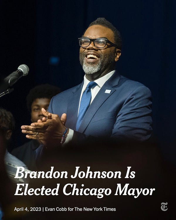 Brandon Johnson clasps his hands in front of him as he celebrates his victory. He wears a blue suit and smiles. White text reads: "Brandon Johnson Elected Chicago Mayor." Photo credit: Evan Cobb for The New York Times