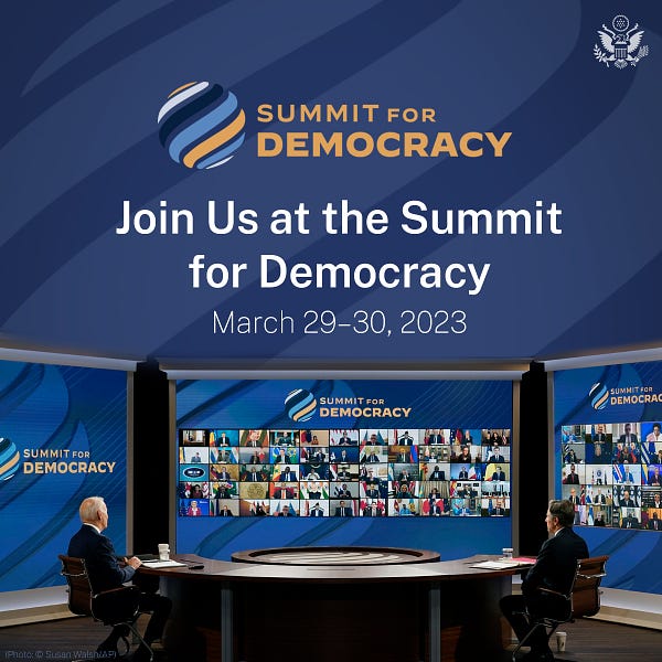 President Biden and Secretary Blinken attend the Summit for Democracy virtually.  They sit at a desk and look at a large screen showing other participants.  The text reads: Summit for Democracy Join Us at the Summit for Democracy March 29-30, 2023