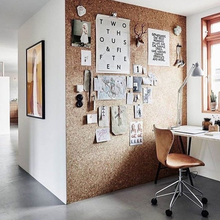 a floor to ceiling rall of cork with a small elegant desk and chair bext to a cork board covered in articles and string pinned and tied to various points all over the board