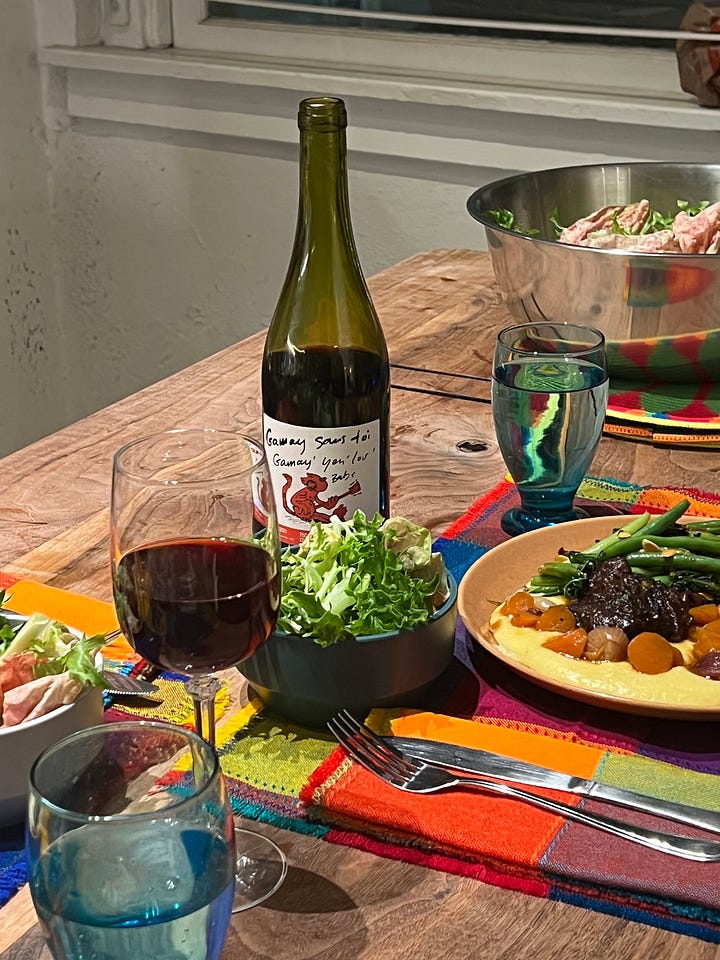 Picture 1: dinner table set with short rib and polenta dinner, bottle of wine set at the center of the table. Picture 2: a woman holding a bottle of French Gamay wine. 