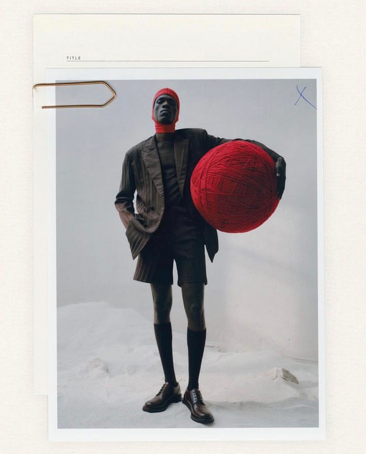 Gottlieb’s artwork depicts a red sphere with a pink halo on the top of the page over a black stain with multiple brushsttrokes coming out of it over a cream coloured background. in the other picture, the model is dressed in black blazer and shorts and red balaklava holding a big red ball against a greyish background