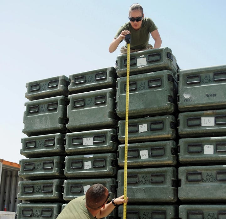 Sgt. Ginni Stalker crouched above a pallet of cargo while taking measurements