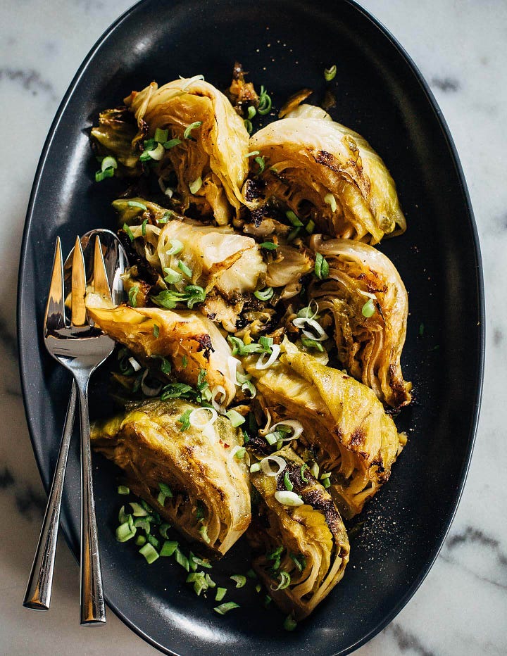 A platter with briased cabbed wedges on the left, and a platter of tacos with golden baked fish, cabbage, and avocado sauce on the right.