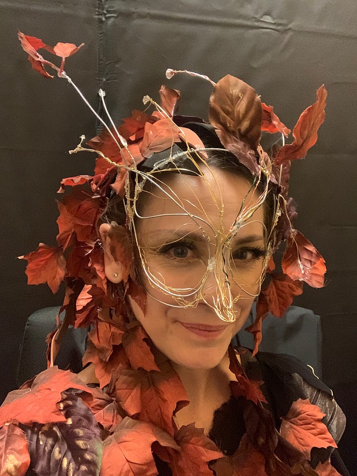 Susan Derry as The Witch in a wire and leaf headdress mask; Cree Carrico in  concert dress holding a program with Susan Derry's bio in it.