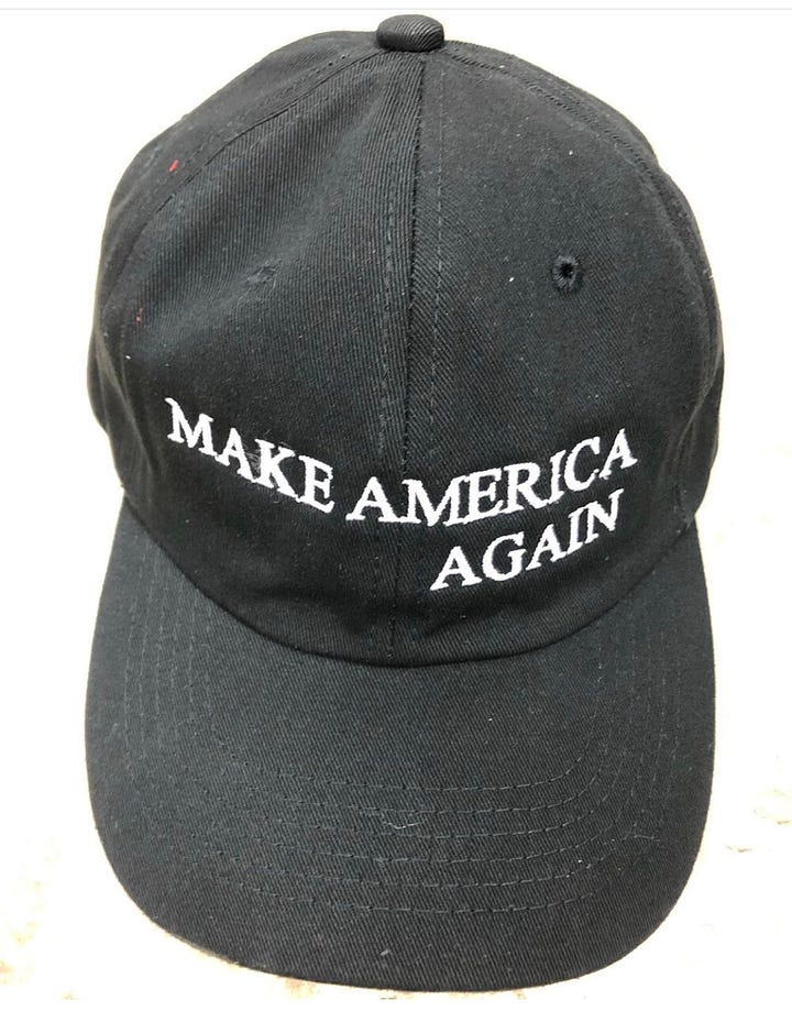 white t-shirt with blue and red A4D logo; dark baseball cap that reads Make America Again