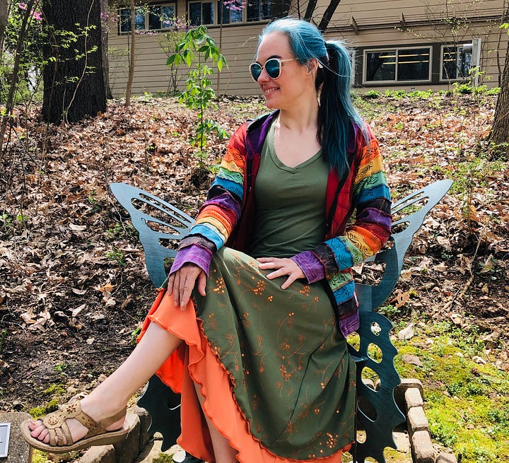 The author in a rainbow striped hoodie and turquoise hair, sitting on a butterfly chair. And kneeling in the multi-color patchwork hoodie with fire-toned hair.