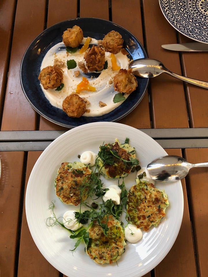 An array of dishes on small plates. Most are composed of spherical items (vegetables chunks or fritters) enhanced with smooth spreads.