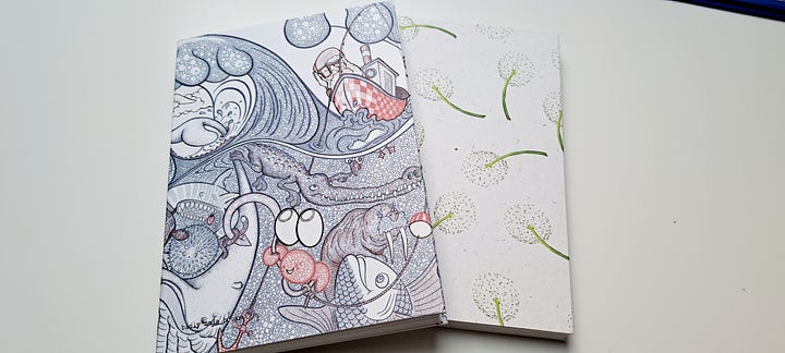 two handmade eco friendly and sustainable notebooks, hand bound and taped, one with a cover of dandelion clocks, one with stylised iamges of waves and the sea.