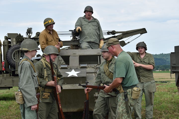 Men dressed in WWII attire stand around a tank that has a big white star on the side.
