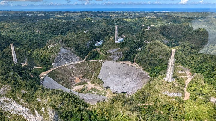 LEFT: Arecibo Observatory is set in forested mountains with the concrete bowl contrasting verdant green. Wires are run between three tall supports strung like a suspension bridge with an array of equipment dangling between the three on lines. RIGHT: The Arecibo Telescope during demolition process, December 2021. Credit: Tedder at Wikimedia Commons (https://commons.wikimedia.org/wiki/File:Arecibo_Telescope,_December_2021.jpg)