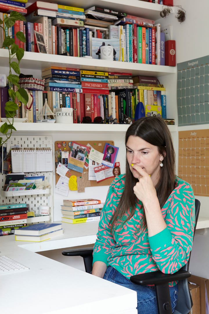 A white woman with a green jumper on sits at a desk working