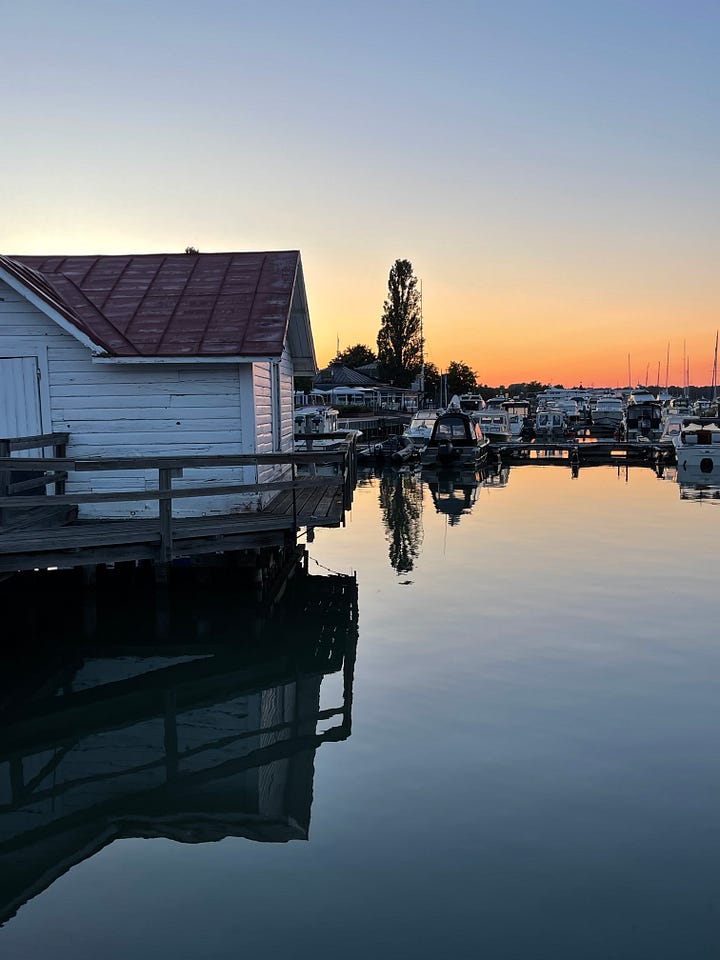 Still harbour water full of sail boats with a dark blue sky and orange light from the sun on the horizon