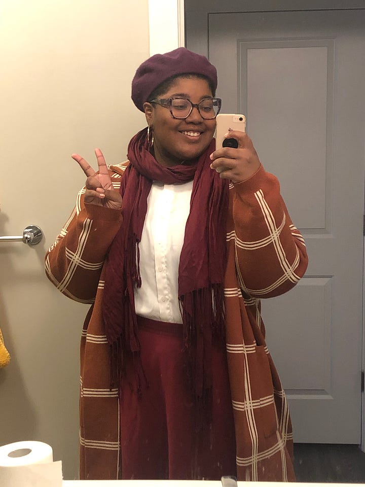 Image 1: Mirror photo of Ravynn in a lilac jumpsuit with a plaid blazer over it and a maroon scarf around her neck; image 2 is Ravynn in a maroon circle skirt and poet sleeve white blouse with a orange plaid cardigan over it and a maroon scarf around her neck and a purple beret on; image 3 is Ravynn in an Ironheart t-shirt, black blazer, and belted jeans; Image 4 is Ravynn in a feminist writers shirt with belted black jeans and a plaid blazer over top.