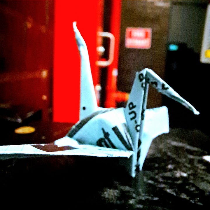 paper cranes folded from some sort of promotional material positioned on a black background in front of a bright red fire hydrant