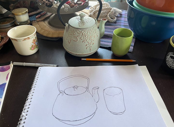 A pad of paper on my table with a black and white line drawing of a teapot and cup. The second image, the drawings are painted with watercolour