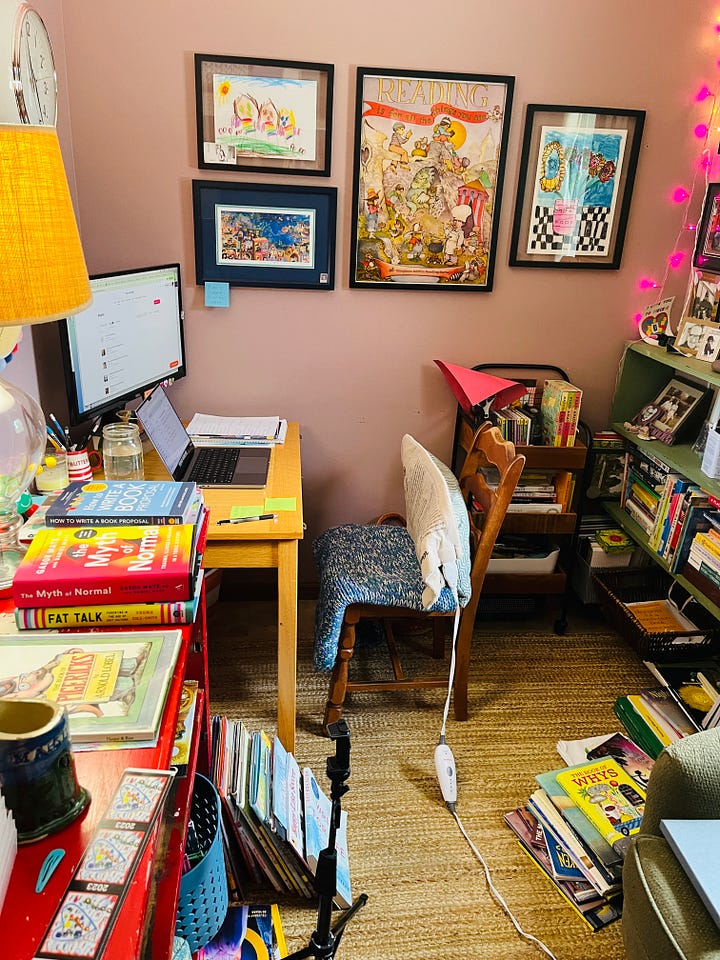 A room with a desk, a bookcase, and a comfortable chair, basically covered with children's books on every surface