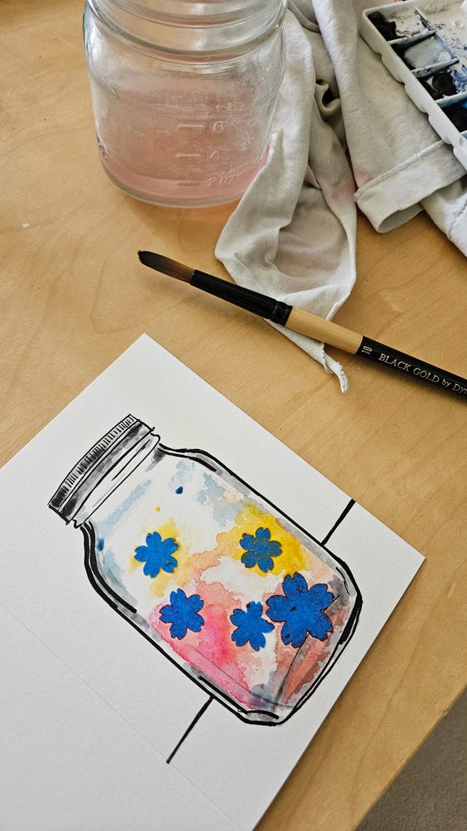 The front of the mason jar card has been painted with blue, yellow and red watercolors over the blue flower-shaped tape masks. A second image shows a detail of fingers peeling off a flower-shaped tape mask.