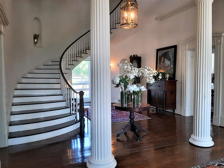 A white column and winding staircase with wood floors, and a room in Long Branch, featuring a fireplace, a cozy chair and oriental rug on the floor.