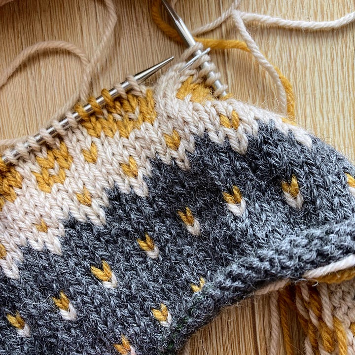 The left image is of an infinity cowl in progress, with nice stranded colourwork motifs. The right image shows five distinct yarns: a natural, a beige, a dark gray, a rust and a mustard coloured.