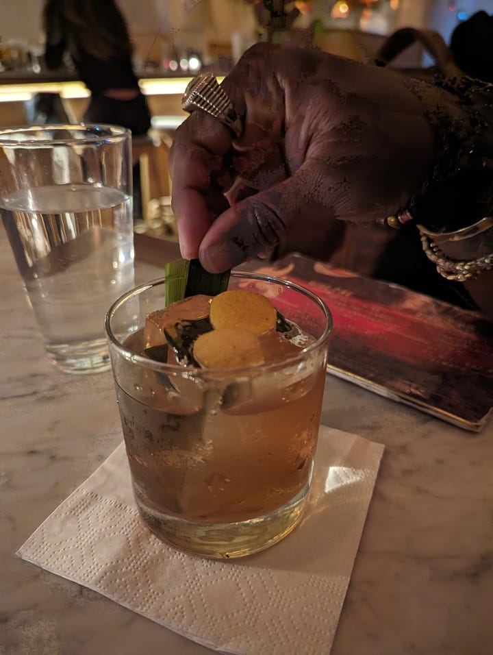 Left: A yellow drink with a sage leaf on top in a glass with a straw tail; Carlos' hand holding a part of his old fashioned, topped with orange peel