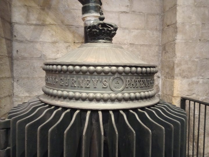 Large, cylindrical stove with slats, with pipe leading to ceiling