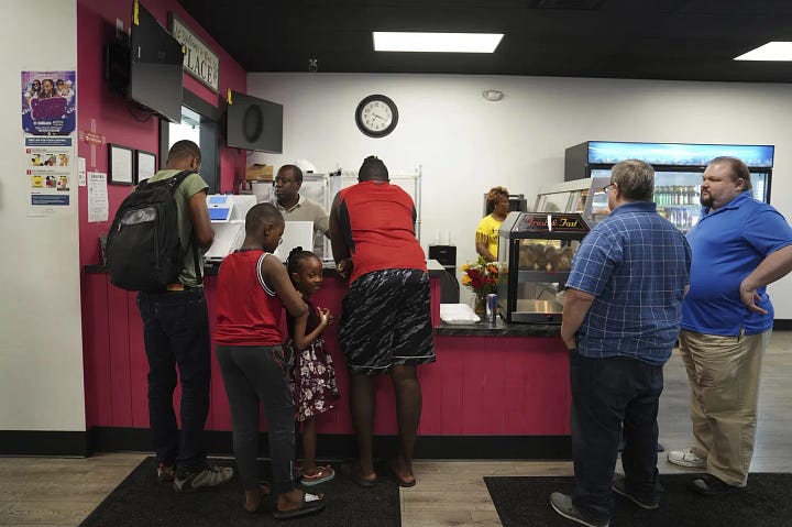 Left: Romane Pierre of Rose Goute Creole Restaurant in Springfield, Ohio, helps a line of customers, Monday, Sept. 16, 2024. Right: Karl Mattila, left, and his wife Linda, of Medway, Ohio, talk with Haitian and longtime Springfield resident Jacob Payen at Rose Goute Creole Restaurant in Springfield. Photo: Jessie Wardarski/AP, Sept. 16, 2024.