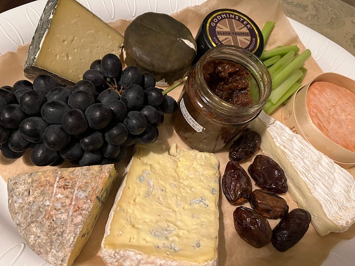 A bowl of lentil & vegetable soup with visible carrots & cavalo Nero plus a cheeseboard with a selection of cheeses plus grapes, dates , celery & chutney