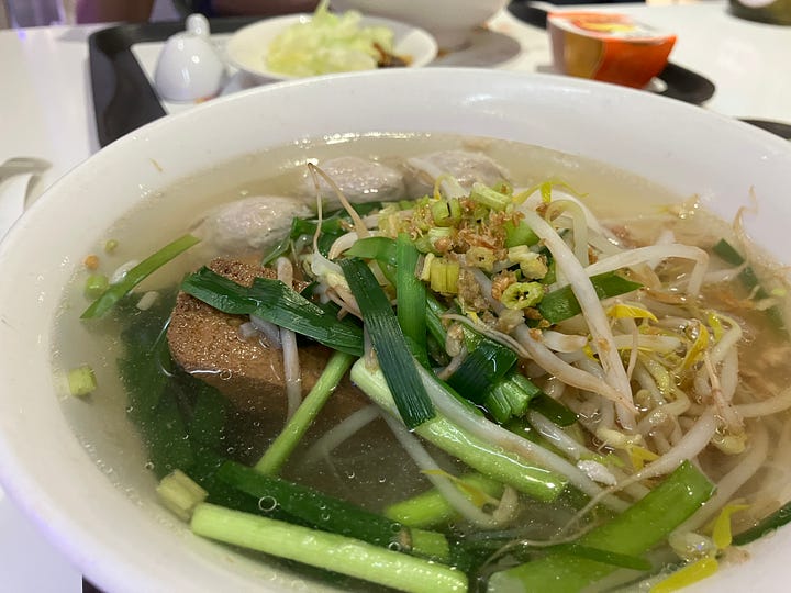 Image on the right depicts two trays of hot noodles. Image on the right is a close-up of a meatball rice noodles topped with scallions.