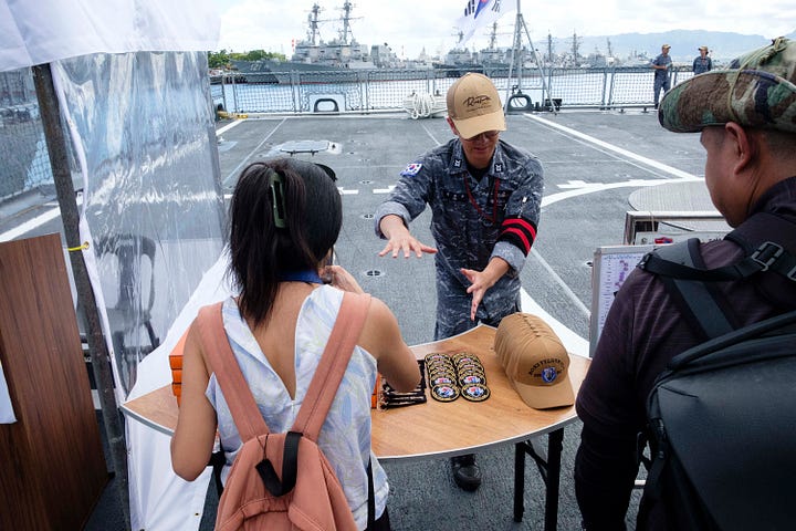 In-port naval open house images including a press conference. One image of the USS Carl Vinson steaming out of Pearl Harbor as a passanger jet takes of at HNL.