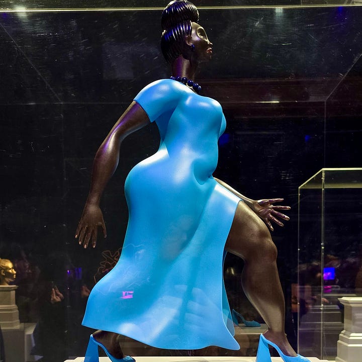 Sculpture of woman in a blue dress striding out and a hollow glass horse and rider sculpture