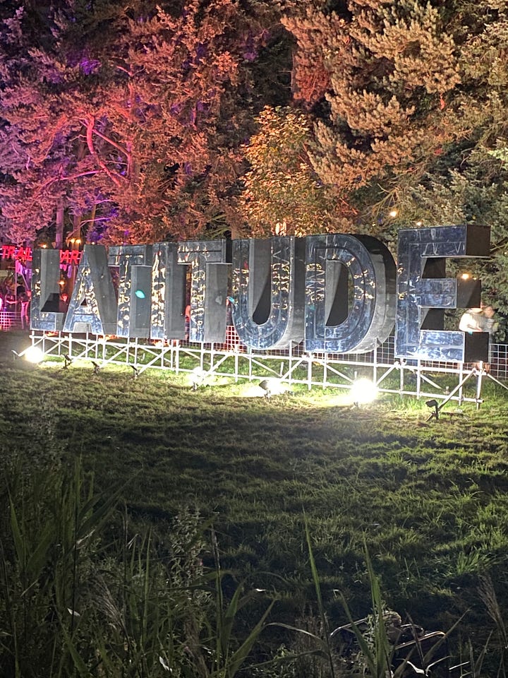 Artistic lighting at latitude festival (large latitude letters in a reflective metal lit up, multi-coloured strips leading into the zen area lit up with giant brightly coloured flowers leading to the entrance, lights strung up between trees in the wood and finally a kaleidoscope dome in gold