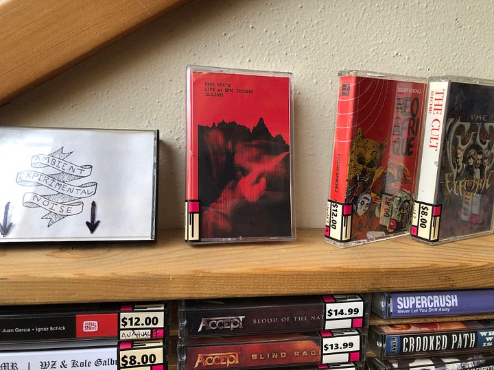 Free Static's new cassette release "Live at Epic Seconds 12.9.2022" pictured on a shelf at Epic Seconds, and in a stack on my drawing table.
