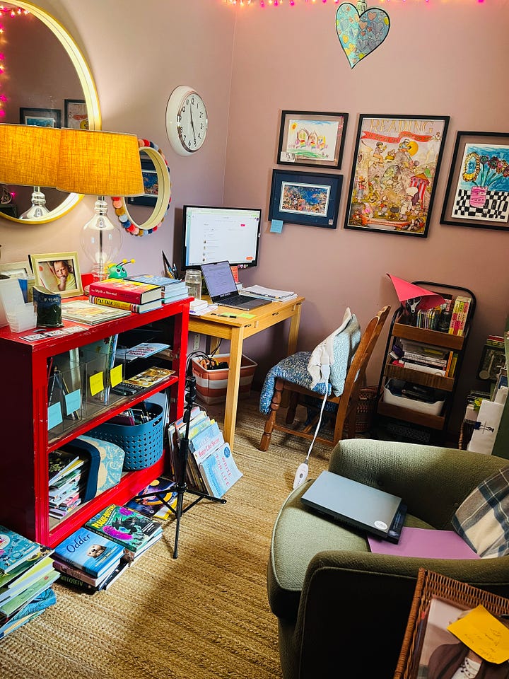 A room with a desk, a bookcase, and a comfortable chair, basically covered with children's books on every surface