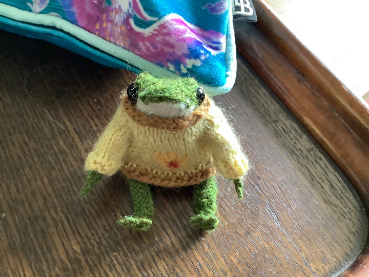 A tiny knitted frog in a cream jumper in a variety of poses, one without the jumpers and looking balletic
