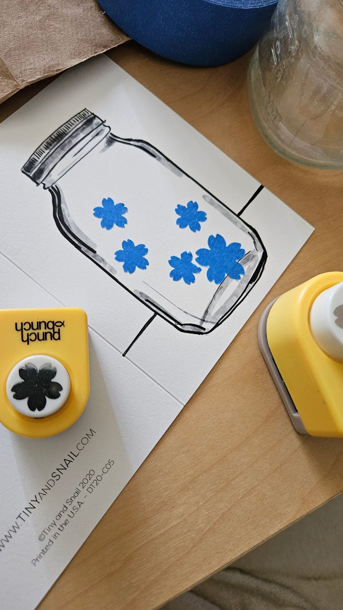 The front of a card with a black pen drawing of a capped mason jar. A second photograph shows blue tape masks cut into flower shapes placed on the front of the card, inside the mason jar drawing.