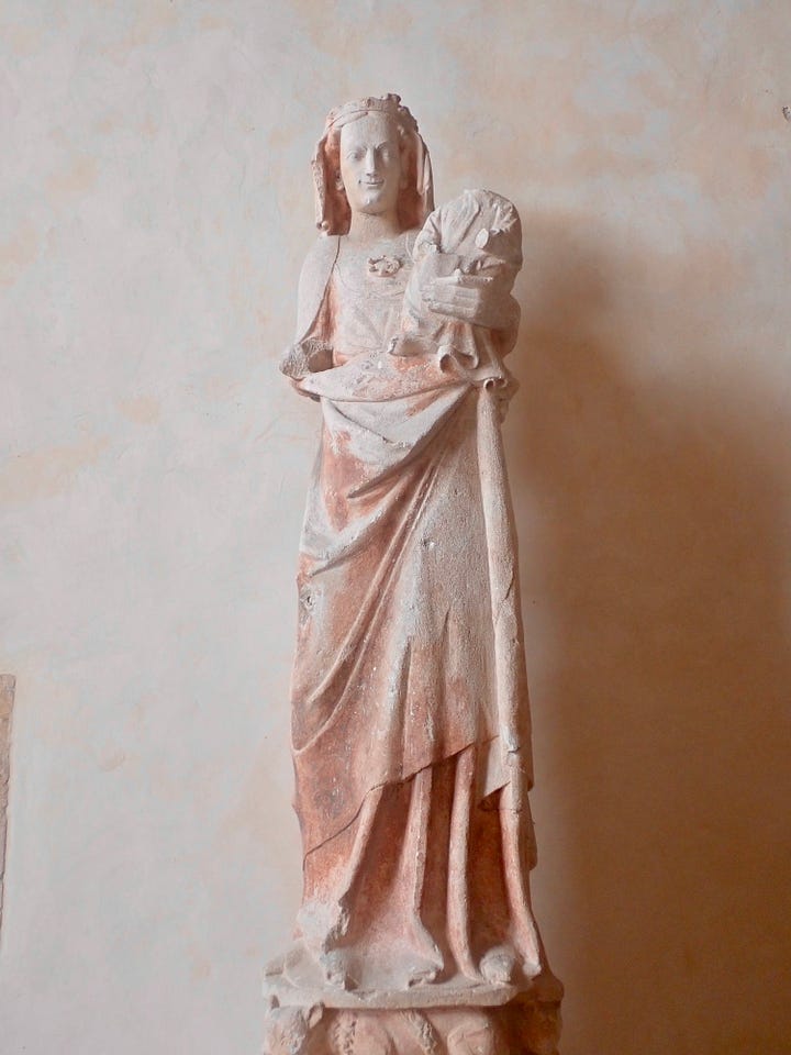 Stone statue of woman holding child with lambs at her feet