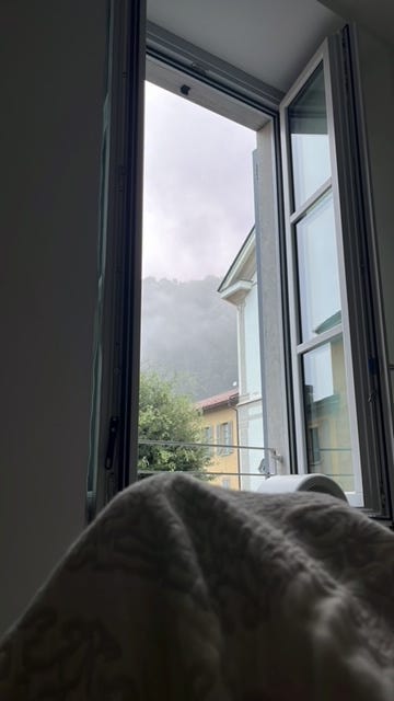 weather radar of rain in italy, open window in a northern italian home with clouds and rain outside and legs under the covers of a bed inside