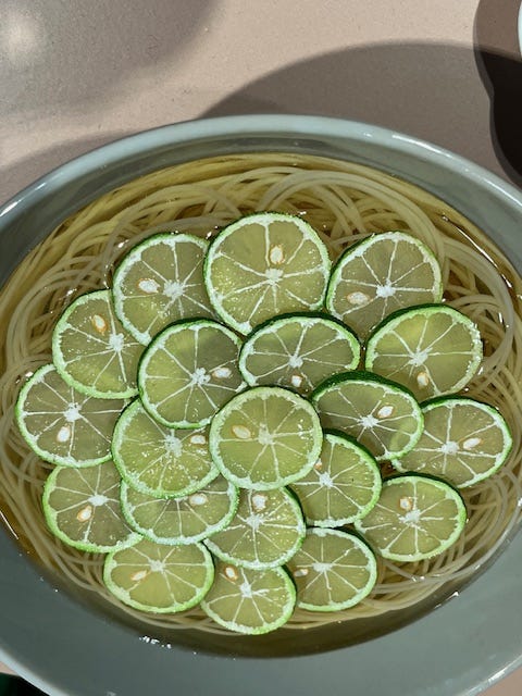 Image on the right is of a a plate of slices of a green, Japanese citrus fruit called Sudachi. On the left is a whole Sudachi, about the size of a lime, with a knobbly skin