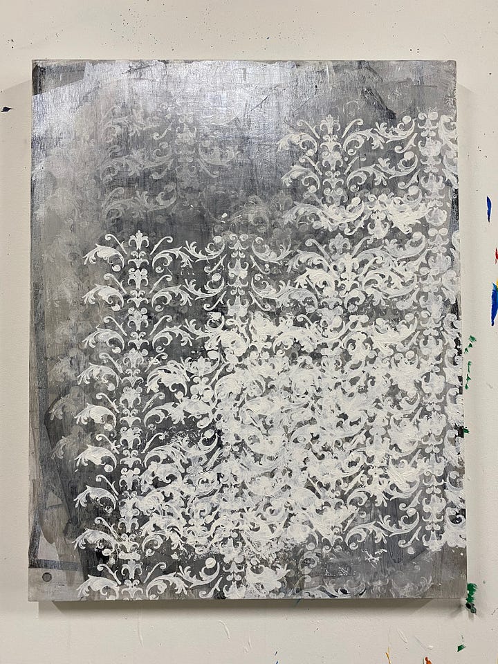 1st photo (left), painting panel on table covered in white paint with a section at the bottom covered in plastic. Second photo: painting with multiple layers of white leafy stencils over a silver acrylic paint background. 