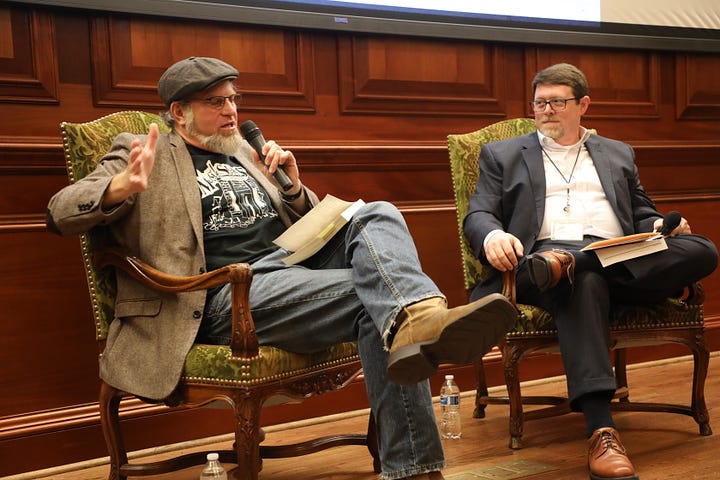 Bob Beatty (left) and Steve Murray (right) sit in chairs. Bob is wearing a hat, a tweed coat with elbow patches, a black Muscle Shoals Sound tshirt, blue jeans, and boots. Steve is in a gray suit with a white shirt. 