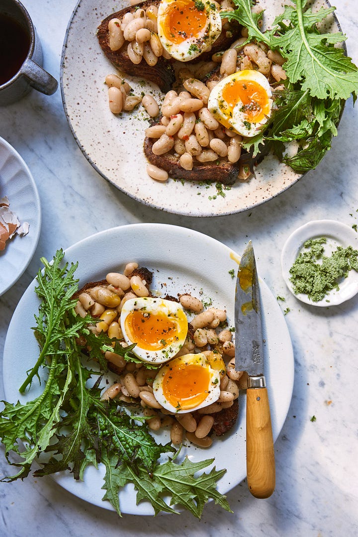 4 images of different plated dishes that Melina cooked and styled. The top left is a fresh pasta with peas, the top right is a cake with bright red plums on top, the bottom left is scallops with asparagus and nasturtiums, and the bottom right is of beans on toast with arugula and a jammy egg opened up on top 