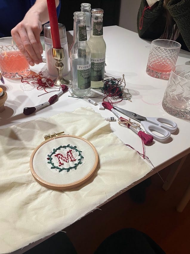 charcuterie board with many meets, crackers, cheeses,etc; embroidery project on table that shows a 'M' with a wreath around it