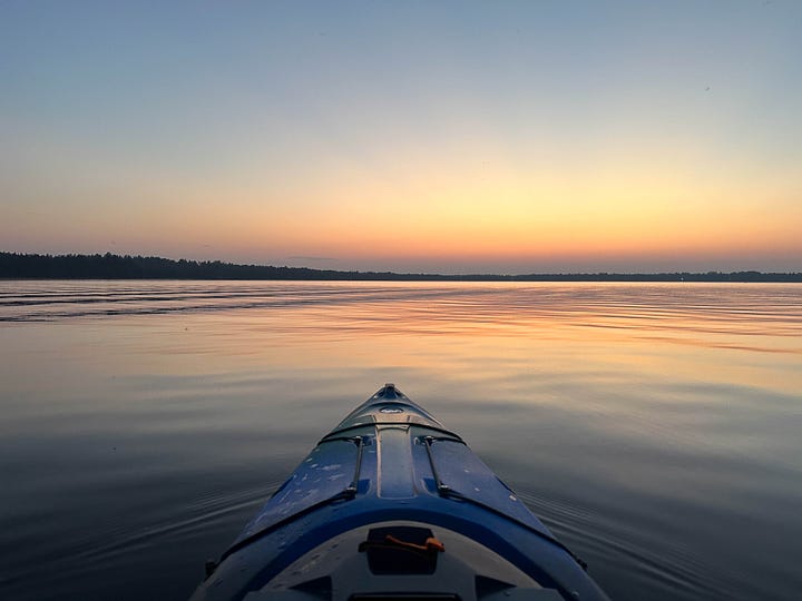 Bike lying on a rock by a lake. Kayak point floating into the sunset.